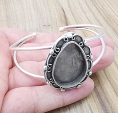 a hand holding a silver bracelet with a stone in it