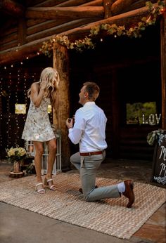 a man kneeling down next to a woman in front of a wooden structure with string lights