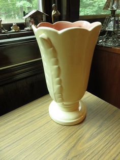 a large white vase sitting on top of a wooden table next to a windowsill