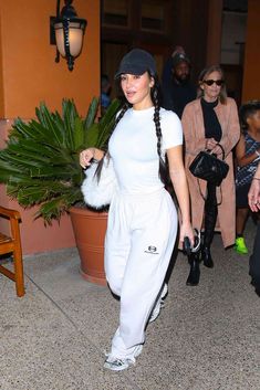 a woman in white is walking down the street with her hand on her hip bag