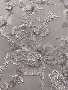 an embroidered fabric with flowers and leaves on the bottom, is shown in grey color