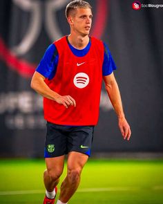 a man in red and blue shirt running on a field with soccer ball behind him