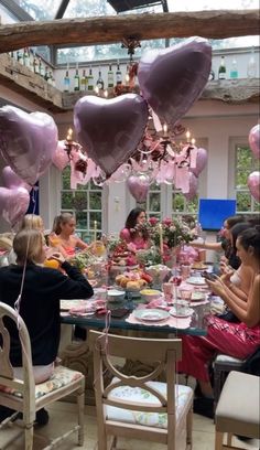 a group of people sitting around a table with heart shaped balloons hanging from the ceiling