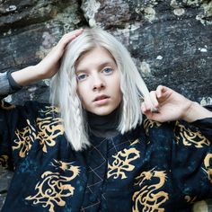 a woman with blonde hair and blue eyes poses for a photo in front of a rock wall