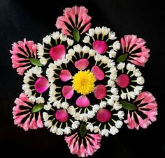 a circular arrangement of pink and white flowers on a black surface with yellow center surrounded by petals