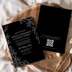 two black and white wedding cards sitting on top of a wooden tray next to flowers