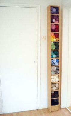 a wooden shelf filled with balls of yarn next to a white wall and door in an empty room