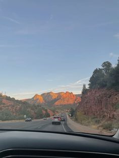 the view from inside a car looking at mountains and trees in the distance with cars driving down the road