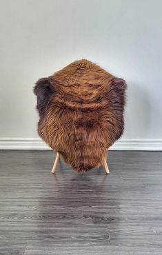 a brown and black furry stool sitting on top of a hard wood floor next to a white wall