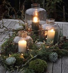 candles are lit in glass jars with moss and pine cones on the table next to them