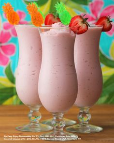 three glasses filled with pink smoothie and topped with strawberries on the rims