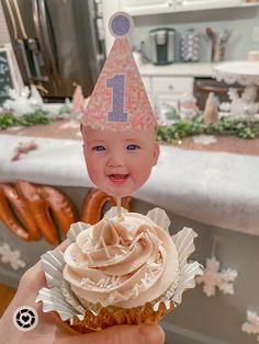 a hand holding a cupcake with frosting and a birthday hat on it's head