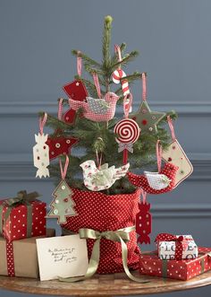 a christmas tree decorated with red and white ornaments on a wooden table next to presents