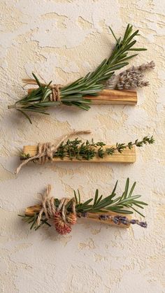 three wooden sticks with herbs tied to them on a table next to a white wall