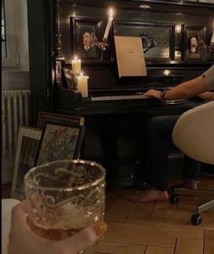 a person sitting at a piano with a glass in front of them and candles on the table