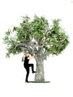 a woman standing next to a tree on top of a white ground with her arms in the air