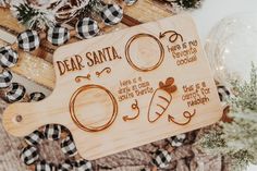 a wooden cutting board with the words dear santa on it and some decorations around it