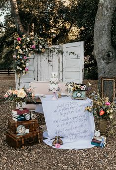 an outdoor ceremony setup with flowers, books and a sign on the ground next to a tree