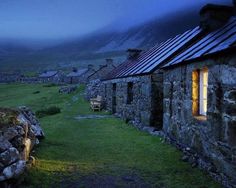 an old stone house in the mountains at night with its lights on and windows lit up