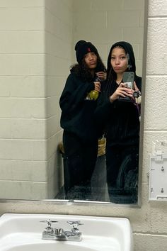 two women are standing in front of a bathroom mirror taking a selfie with their cell phone