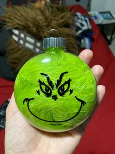 a hand holding a green ornament with a face drawn on it