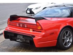 the rear end of a red sports car parked on the side of the road next to other cars