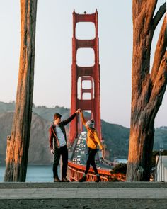 two people holding hands in front of the golden gate bridge