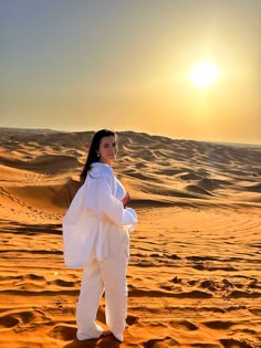 a woman standing in the desert at sunset