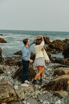 a man and woman standing on rocks near the ocean with their arms around each other