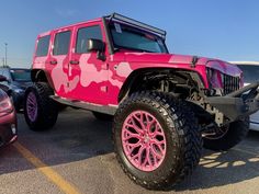 a pink jeep parked in a parking lot next to other cars with camouflage paint on them