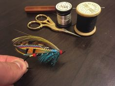 a hand is holding a needle, scissors and spools of thread on a table