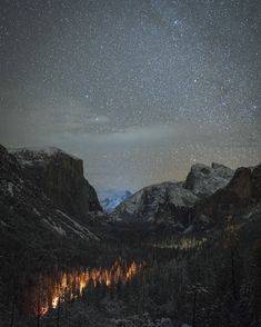 the night sky is filled with stars above mountains and trees in the foreground are snow - capped mountains