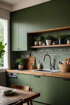 a kitchen with green cabinets and plants on the counter top, along with a wooden dining table