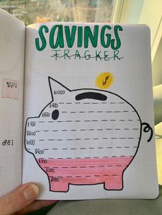 a hand holding up a notebook with a pig on it's cover that says savings tracker