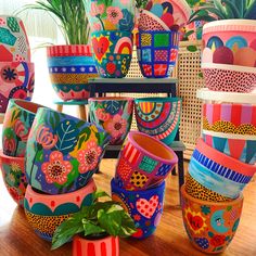 many colorful vases are stacked on top of each other in front of a potted plant