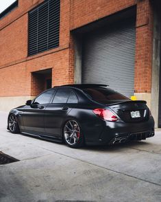 a black car parked in front of a brick building next to a parking garage door