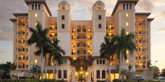 a large hotel with palm trees and lights on it's front entrance at dusk