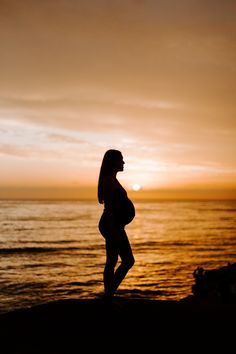 a pregnant woman standing on the beach at sunset