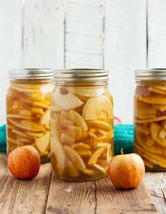 three jars filled with apples sitting on top of a wooden table next to an apple