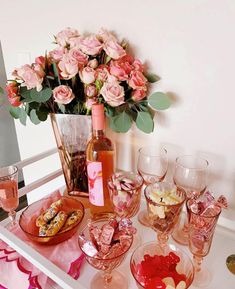 a table topped with lots of glasses filled with wine and food next to a vase full of pink roses