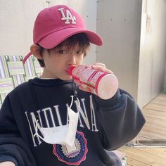 a young boy sitting on a chair drinking from a bottle while wearing a pink hat