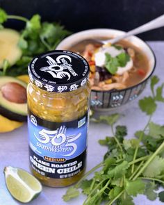 a jar of salsa next to some cilantro, limes and avocado