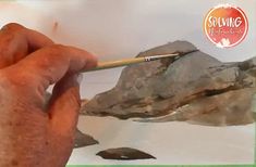 a man is painting rocks with a brush and watercolors on the paper in front of him