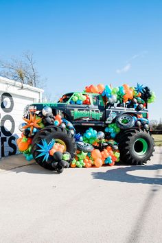 a monster truck decorated with balloons in the shape of flowers and stars is parked next to a garage