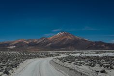 a dirt road in the middle of nowhere with mountains in the background and blue sky