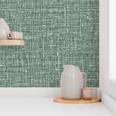 two white vases sitting on top of a counter next to a green wallpaper