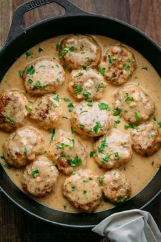 a skillet filled with meatballs and gravy on top of a wooden table