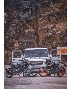 a man standing on the back of a silver truck next to two black and orange motorcycles