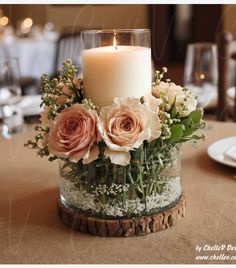 a candle that is sitting on top of a table with flowers and greenery in it