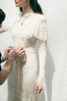 a woman in a white dress is being fitted with a beige ribbon by a man